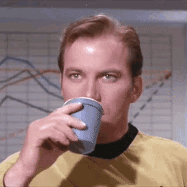 a man is drinking from a blue cup while wearing a yellow shirt