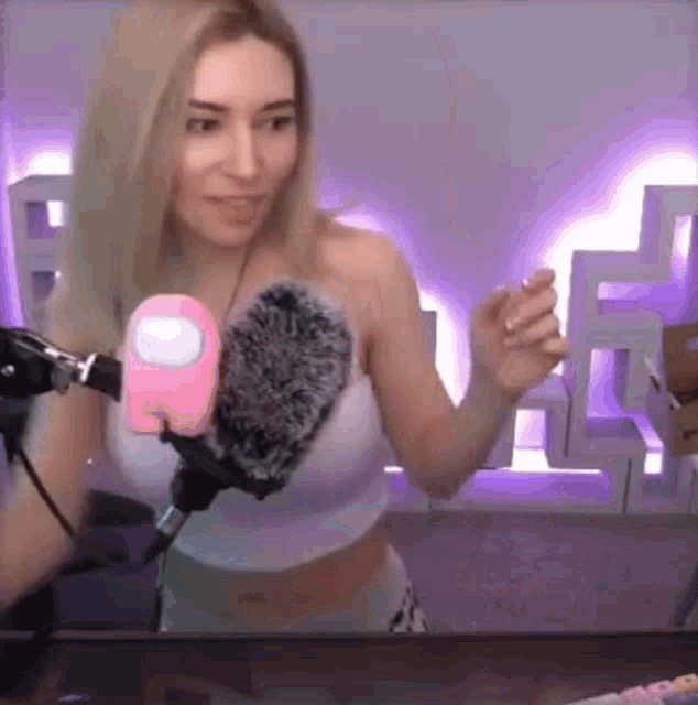 a woman is standing in front of a microphone holding a pink among us .