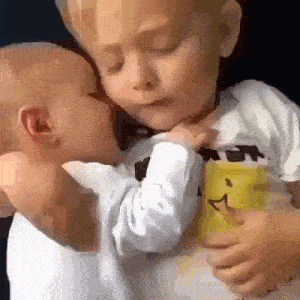 a little boy is holding a baby in his arms and the baby is kissing the boy on the forehead .
