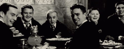 a group of young men are sitting at a table eating food and laughing .
