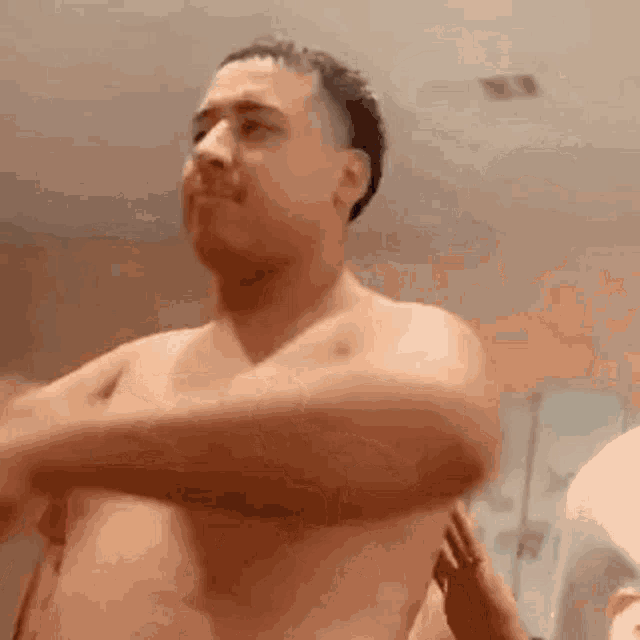 a shirtless man is standing in a room with his hands on his chest .