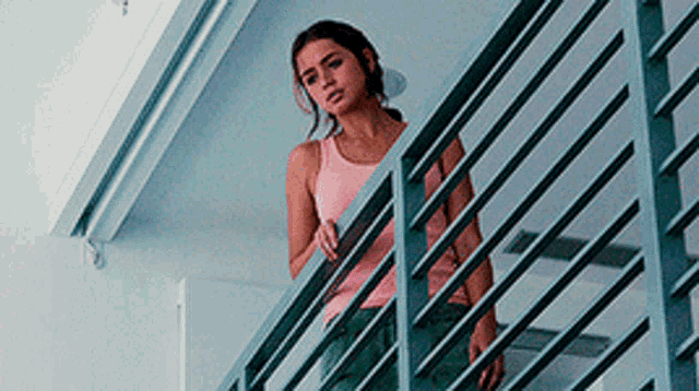 a woman in a pink tank top standing on a balcony