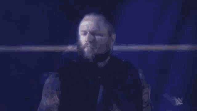 a man with a beard is standing in a wrestling ring in a dark room .