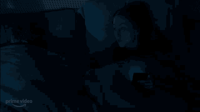 a man and a woman are laying in bed at night looking at a cell phone .