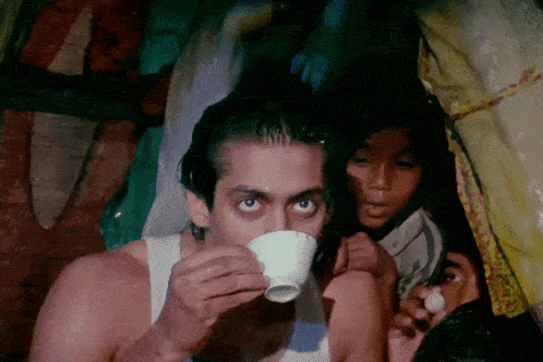 a man in a white tank top drinks from a small cup