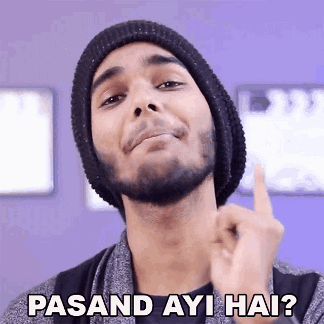 a man with a beard wearing a black beanie is pointing up with the words pasand ayi hai written below him