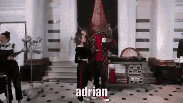 a man and a woman are standing next to each other in a room with the name adrian on the floor .