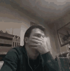 a man is covering his mouth with his hand while sitting at a table in a room .