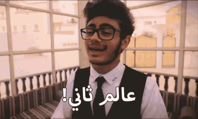 a man wearing glasses and a vest says " عالم ثاني " in arabic
