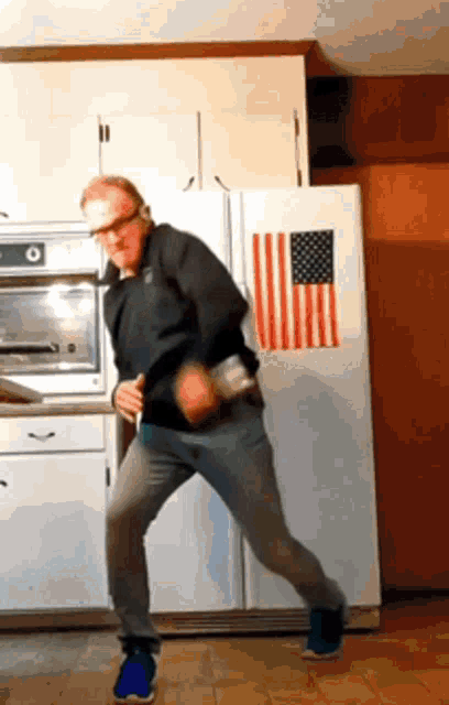 a man is dancing in a kitchen in front of an american flag