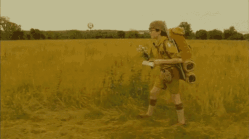 a man with a backpack is walking through a field holding a bouquet of flowers .