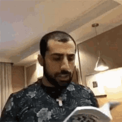a man with a beard is reading a book while wearing a floral shirt .
