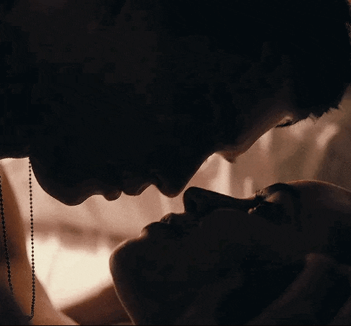 a man and a woman are kissing in the dark and looking at each other .