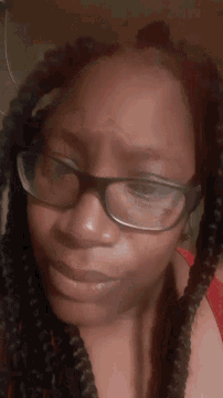 a woman wearing braids and glasses looks down at something