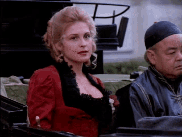 a woman in a red dress is sitting in a carriage with a man in a black hat