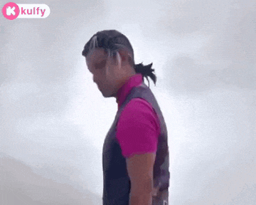 a man in a pink shirt and a purple vest is standing in front of a mountain .