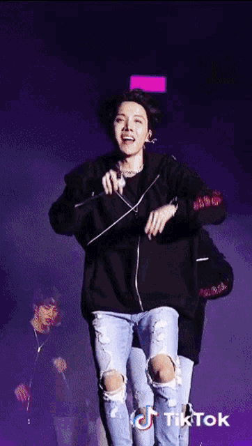a man in a black hoodie and ripped jeans is dancing on a stage with a tiktok logo on the bottom right