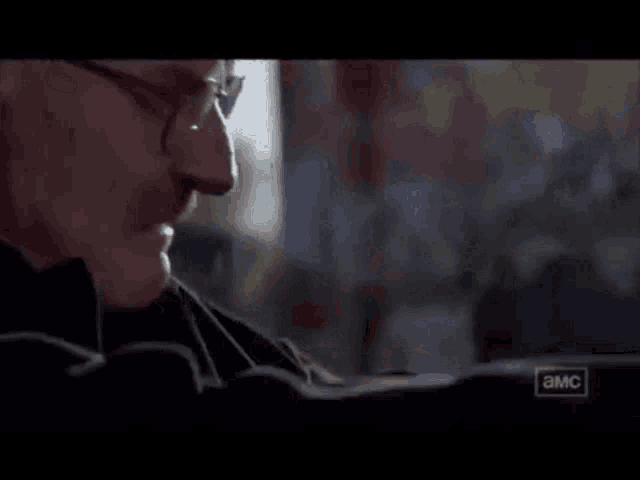 a man wearing glasses is sitting in front of a window and a sign that says ' a.m.c. '
