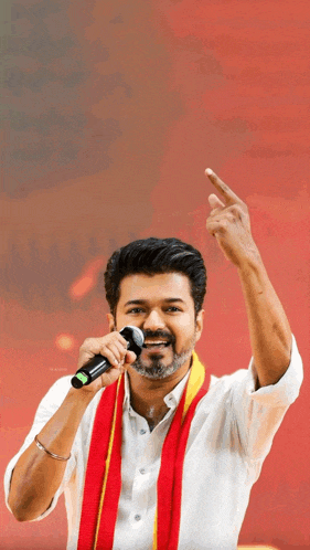 a man in a white shirt and red and yellow scarf is holding a microphone and pointing up .