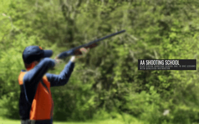 a man is holding a shotgun in front of a sign that says aa shooting school on it