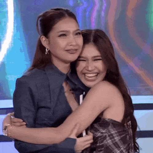 two women are hugging each other and smiling while standing next to each other