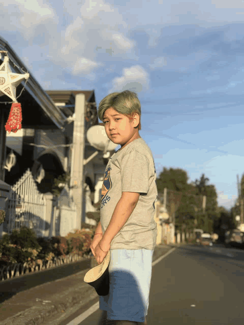 a young boy wearing a gray shirt that says warriors stands in front of a house
