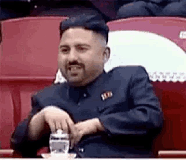 a man in a suit and tie is sitting in a stadium holding a glass of water .