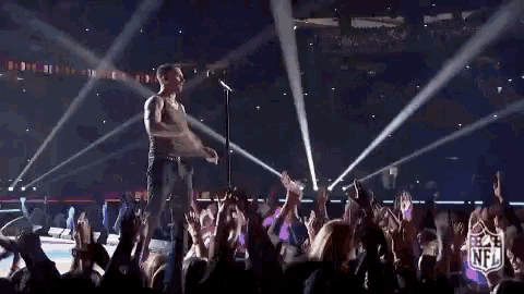 a man without a shirt is singing into a microphone in front of a crowd at a concert .