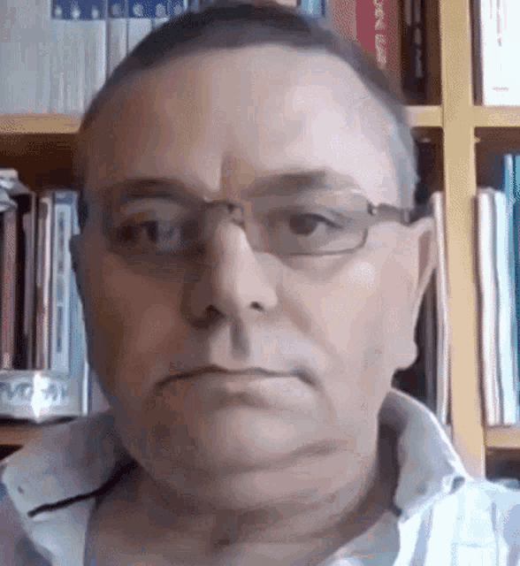 a man wearing glasses is standing in front of a bookshelf