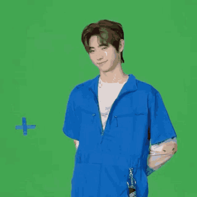 a young man wearing a blue jumpsuit is standing in front of a green screen .