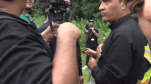 a man in a black shirt is talking to another man in a field
