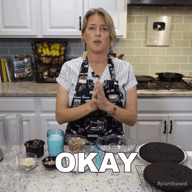 a woman in an apron is standing in a kitchen with the word okay in front of her