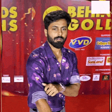 a man in a purple shirt is standing in front of a banner that says ' ds is gold '