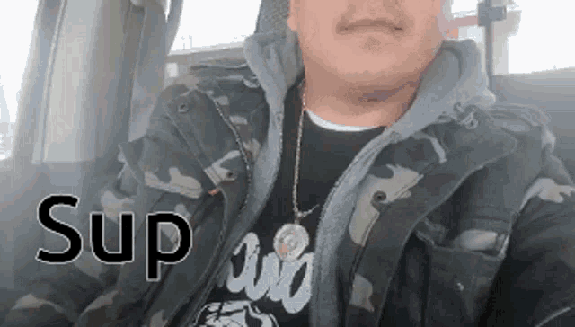 a man wearing a camo jacket and a t-shirt that says sup is sitting in a car