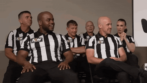 a group of aew referees sit in a row with their arms crossed