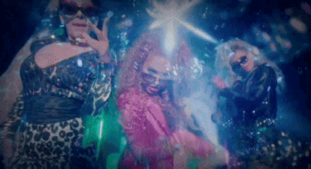 three drag queens are standing next to each other in a dark room .