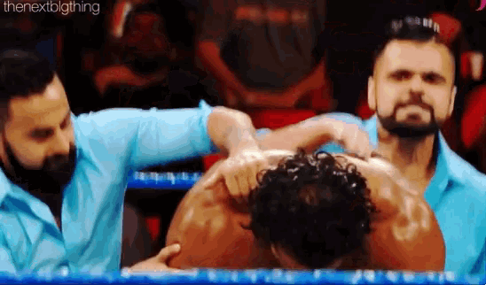 a man with a beard is laying on the ground in a wrestling ring with two other men .