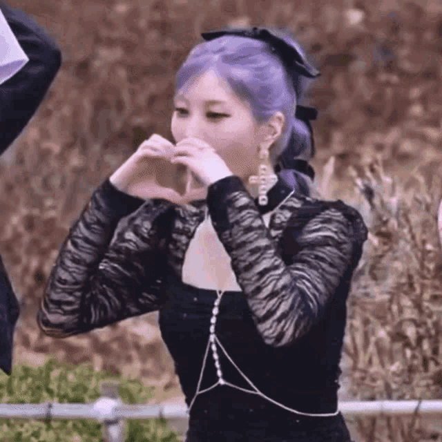 a girl with purple hair is making a heart shape with her hands