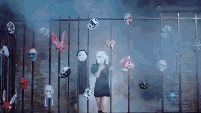 a woman wearing a mask is standing in front of a fence with many masks hanging on it .