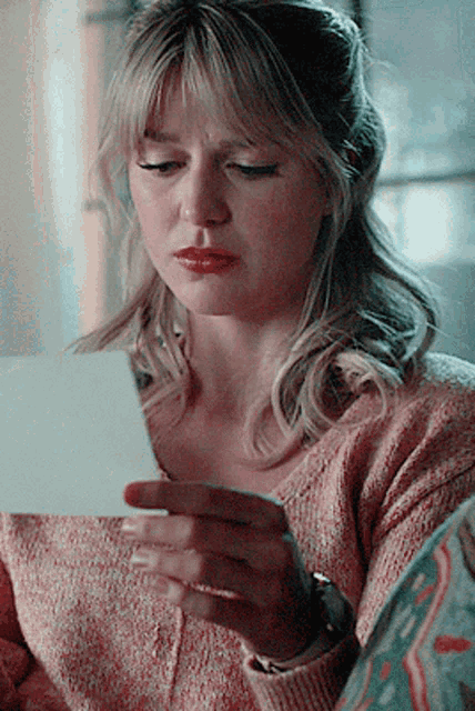 a woman in a pink sweater is holding a piece of paper in her hand