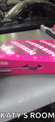 a pink box of dunkin donuts sits on a table next to a car ..