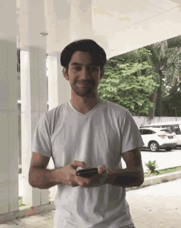 a man in a white shirt is holding a cell phone in his hand