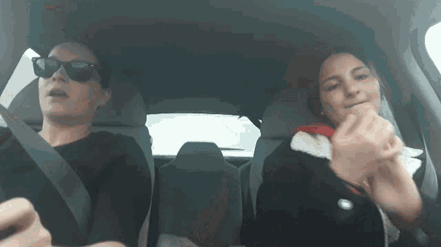 a woman wearing sunglasses is driving a car with another woman in the back seat