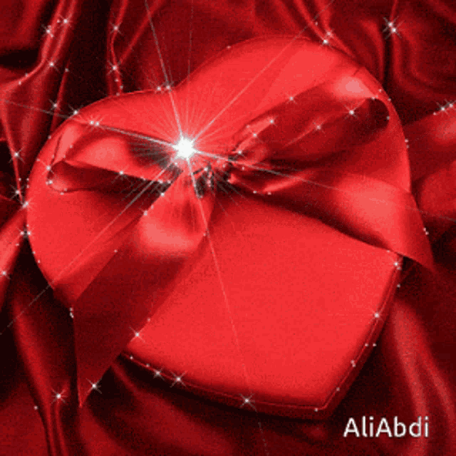 a red heart with a red ribbon is sitting on a red cloth