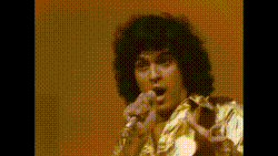 a man with curly hair singing into a microphone with his mouth open