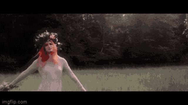 a woman with red hair and a flower crown on her head is walking in a field .