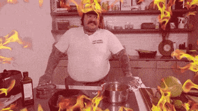 a man wearing a white shirt that says ' chef ' on it is cooking in a kitchen surrounded by flames