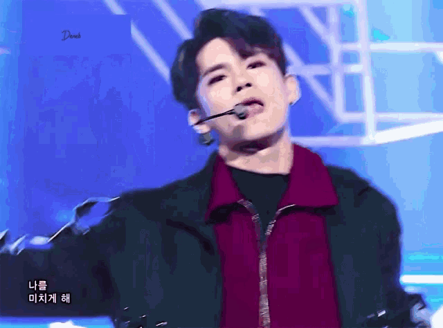 a young man wearing a green jacket and a red shirt is singing into a microphone while standing on a stage .