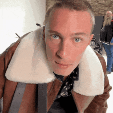 a man wearing a brown jacket with a white fur collar looks at the camera
