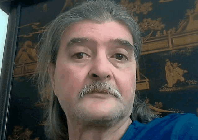 a man with gray hair and a mustache looks at the camera